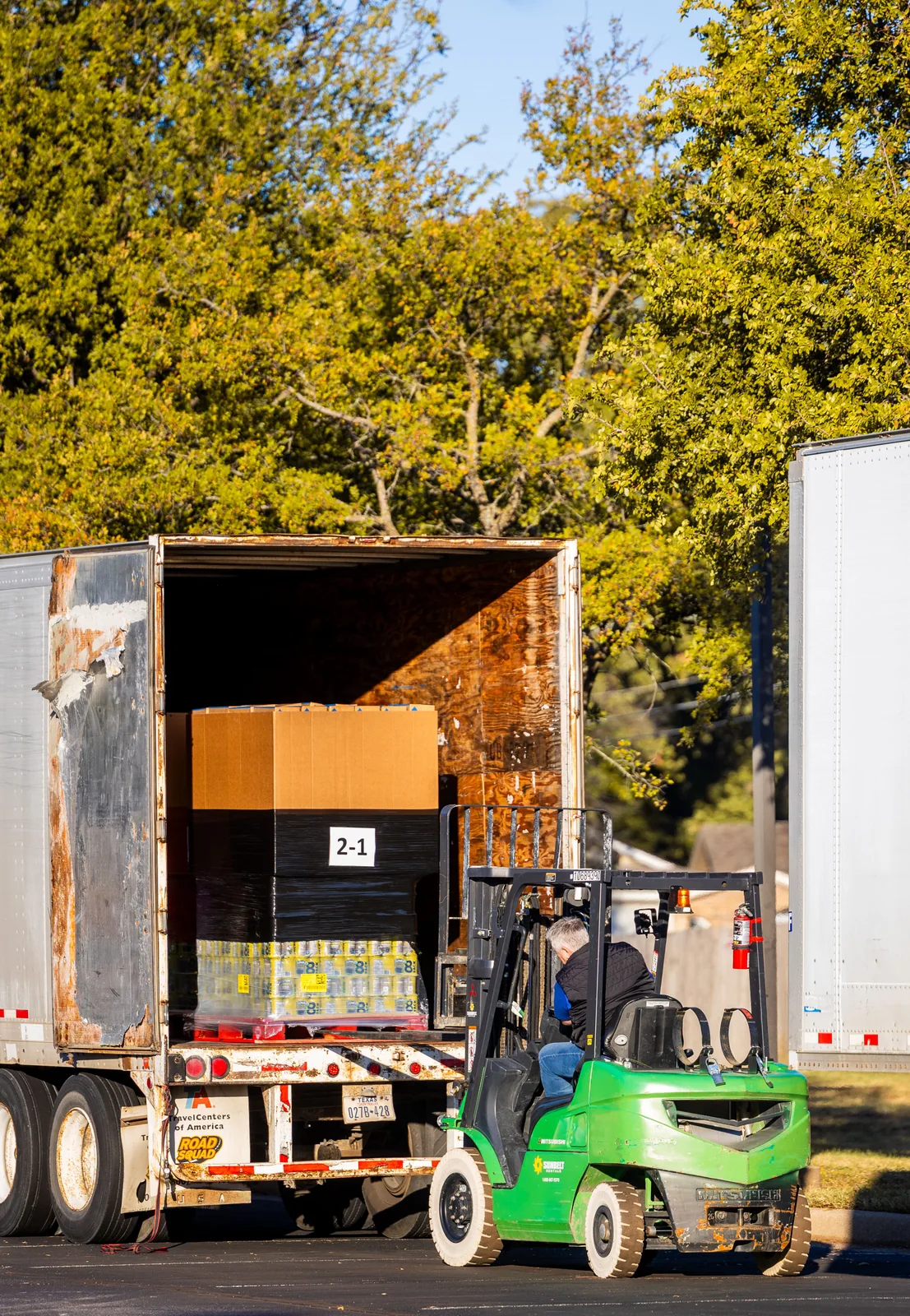 Forklift operator placing a pallet of goods into the open back of a freight trailer